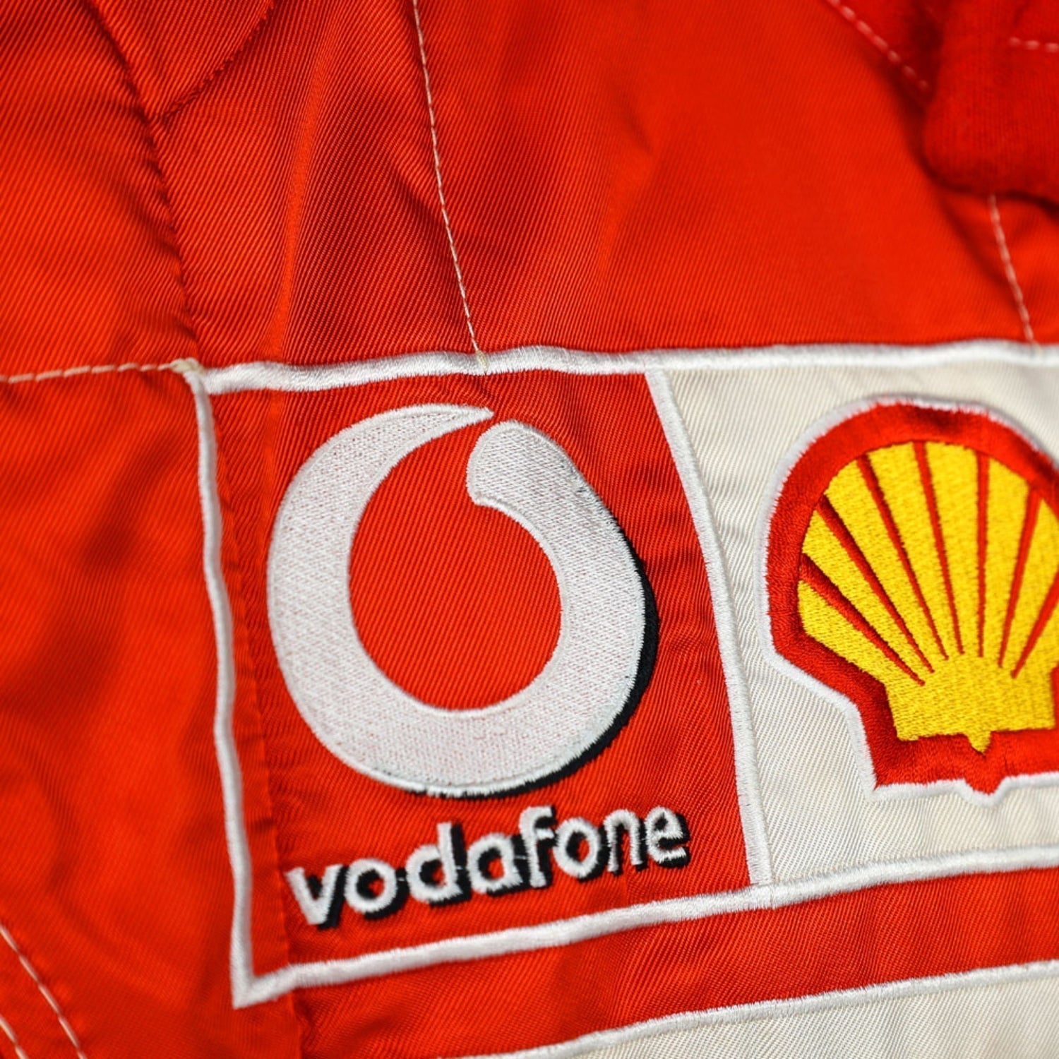 Close-up shot of Schumacher’s 2006 race suit, highlighting the detailed stitching, premium red material, and signature white branding elements.Bestracewear