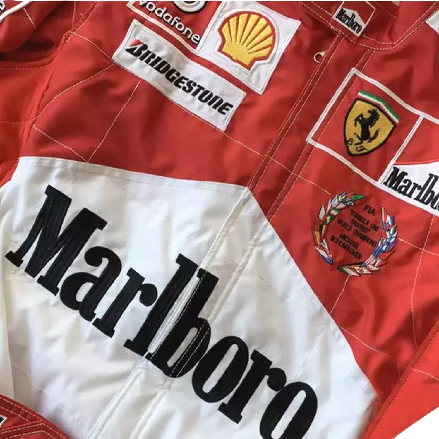 Close-up of the 2005 Schumacher suit highlighting fine embroidery, Ferrari red color tone, and precise stitching on race-worn sponsor badges.Bestracewear
